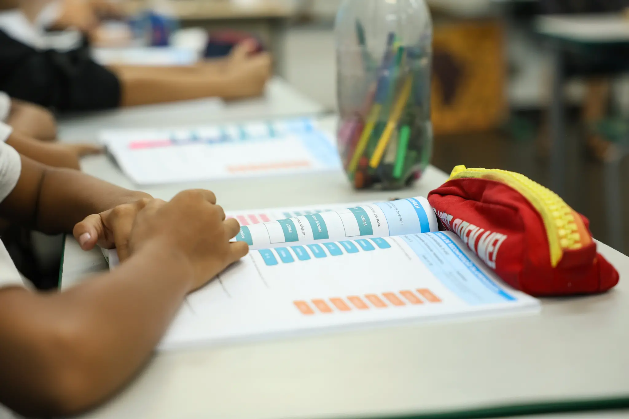 braço de estudante em cima de livro, enquanto assiste aula