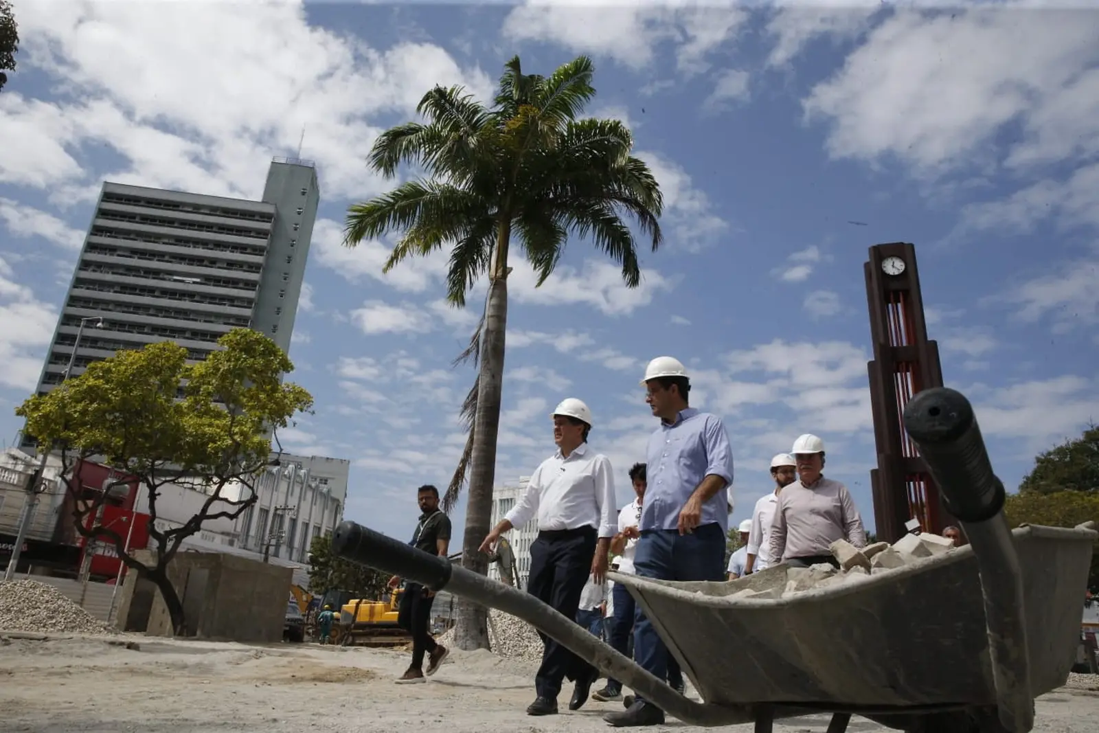 Imagem mostra prefeito Evandro Leitão e equipe visitando as obras de requalificação da Praça do Ferreira, em Fortaleza. Em primeiro plano, aparece um carrinho de mão com materiais de construção. Atrás, as autoridades. Ao fundo, um coqueiro alto e a tradicional Coluna da Hora da praça.