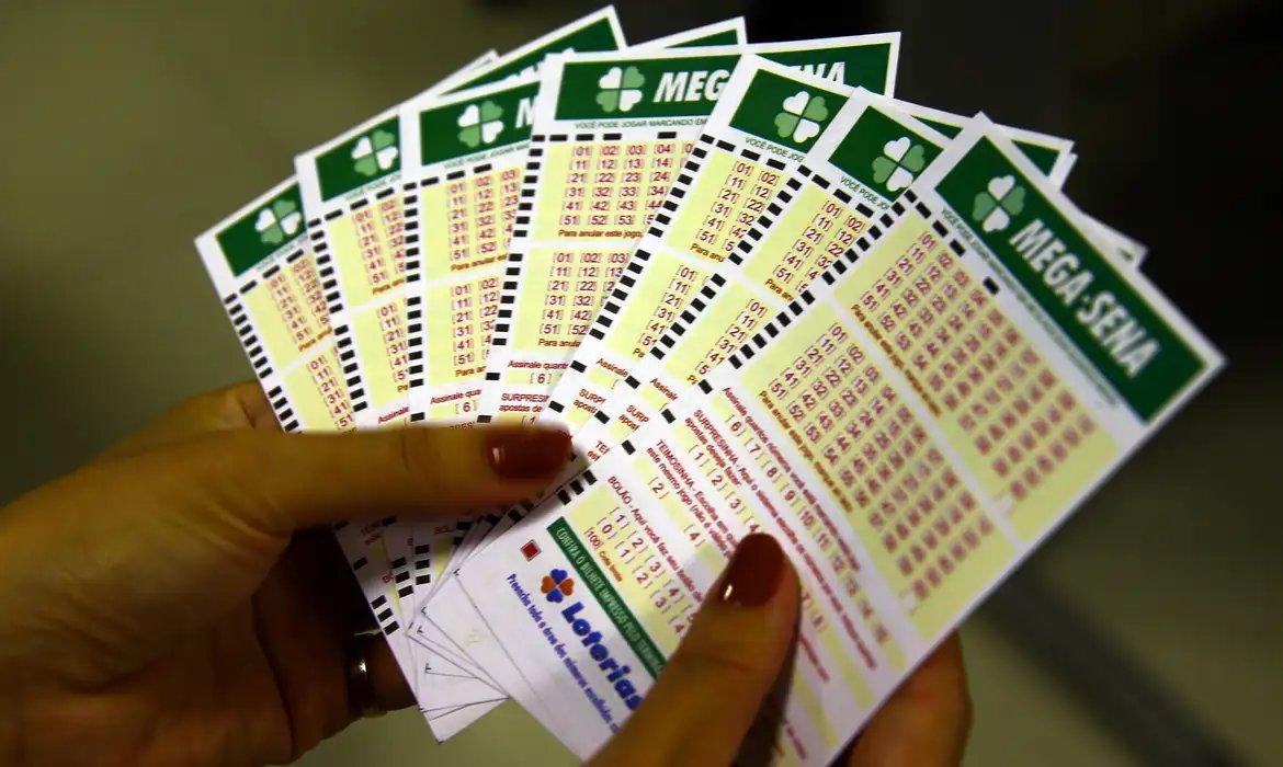 Mãos segurando vários bilhetes de loteria Mega-Sena, prontos para apostar na loteria brasileira, ilustrando loterias do dia com sorteio realizado pela Caixa em 9 de setembro 2025