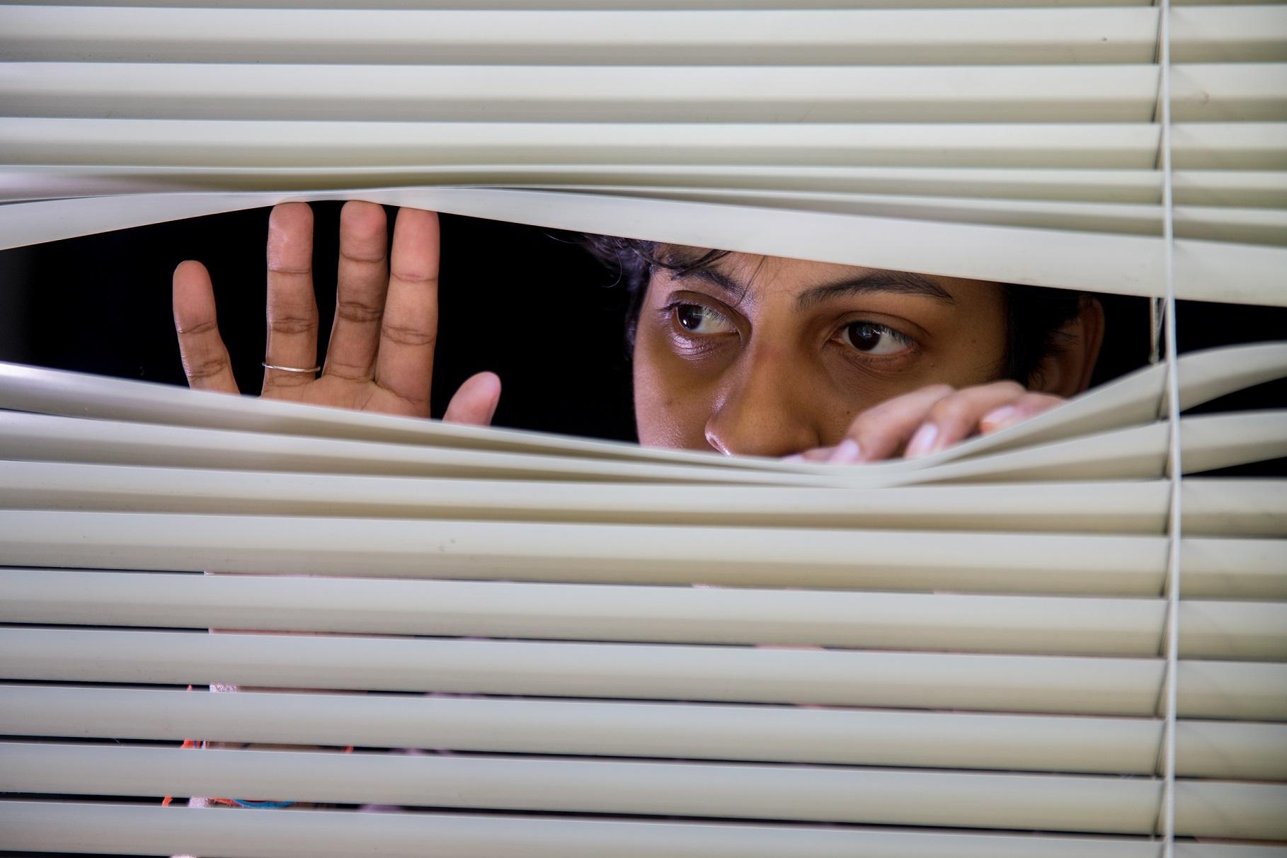 Mulher negra espiando pela fresta de uma persiana branca