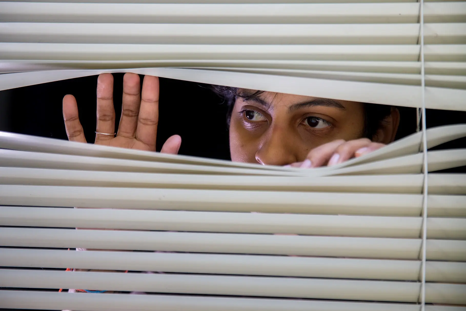 Mulher negra espiando pela fresta de uma persiana branca