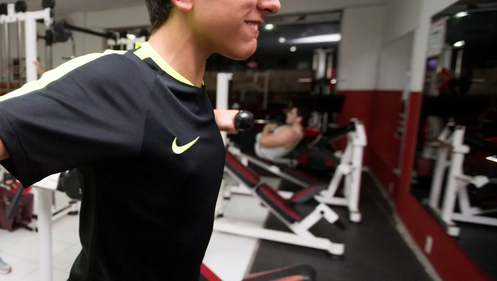 Jovem na academia fazendo exercício de ombros com halteres