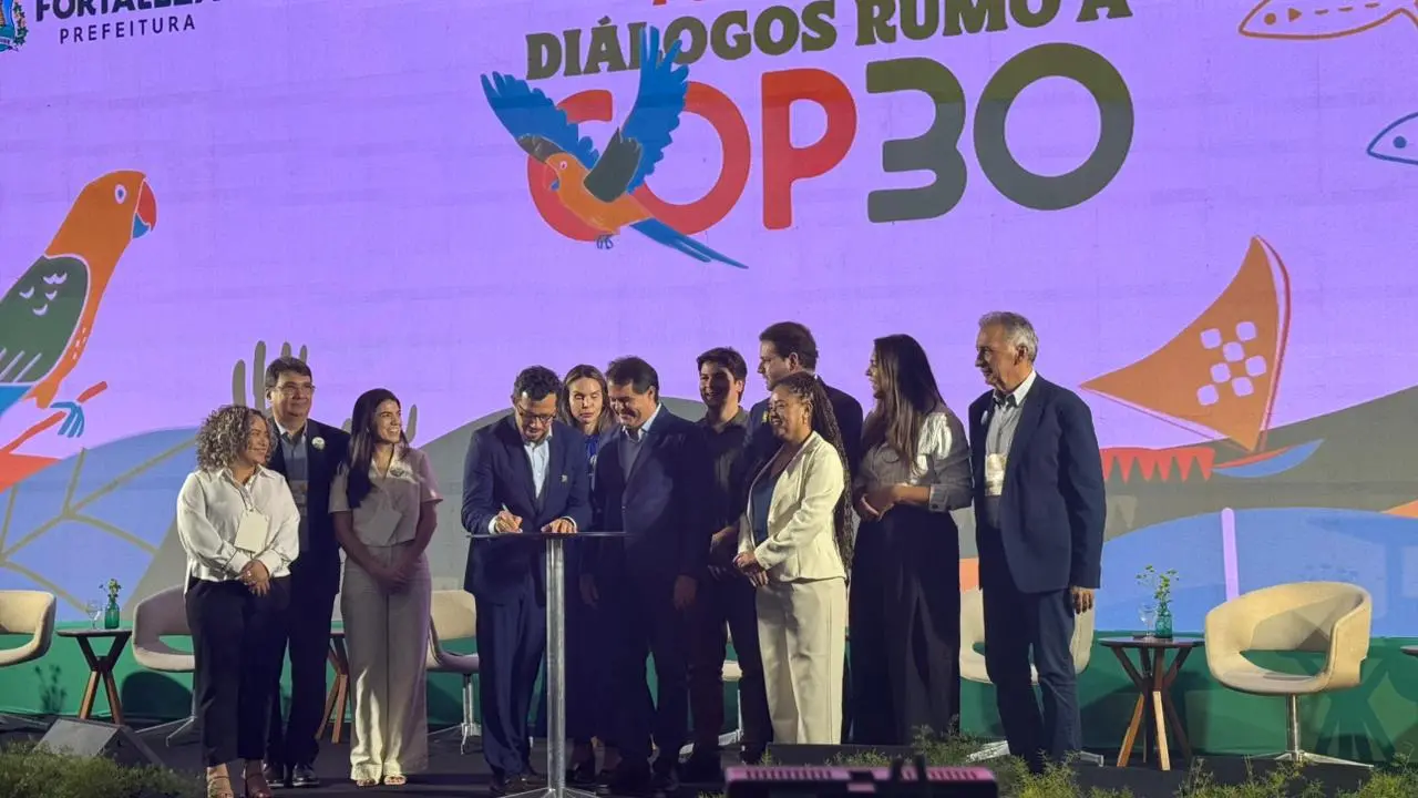 Imagem mostra vários gestores da prefeitura de Fortaleza em cima de palco no centro de eventos do Ceará. Ao fundo, um painel de led mostra a frase Diálogos rumo à COP 30. No logo, um pássaro colorido ilustra a letra C de COP.