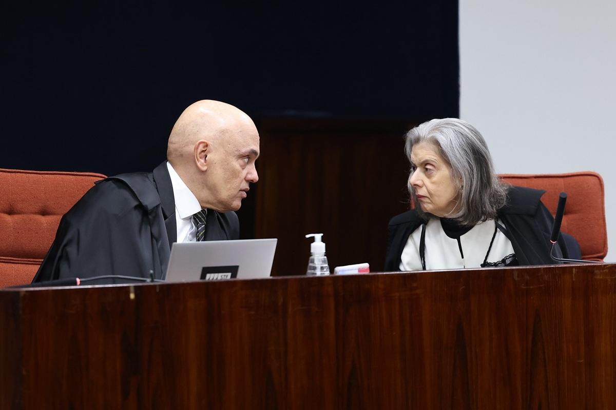 Dois ministros do Supremo Tribunal Federal (STF) conversam durante sessão. À esquerda, um homem de toga preta inclina-se para falar; à direita, uma mulher também de toga preta e roupa clara escuta atentamente.