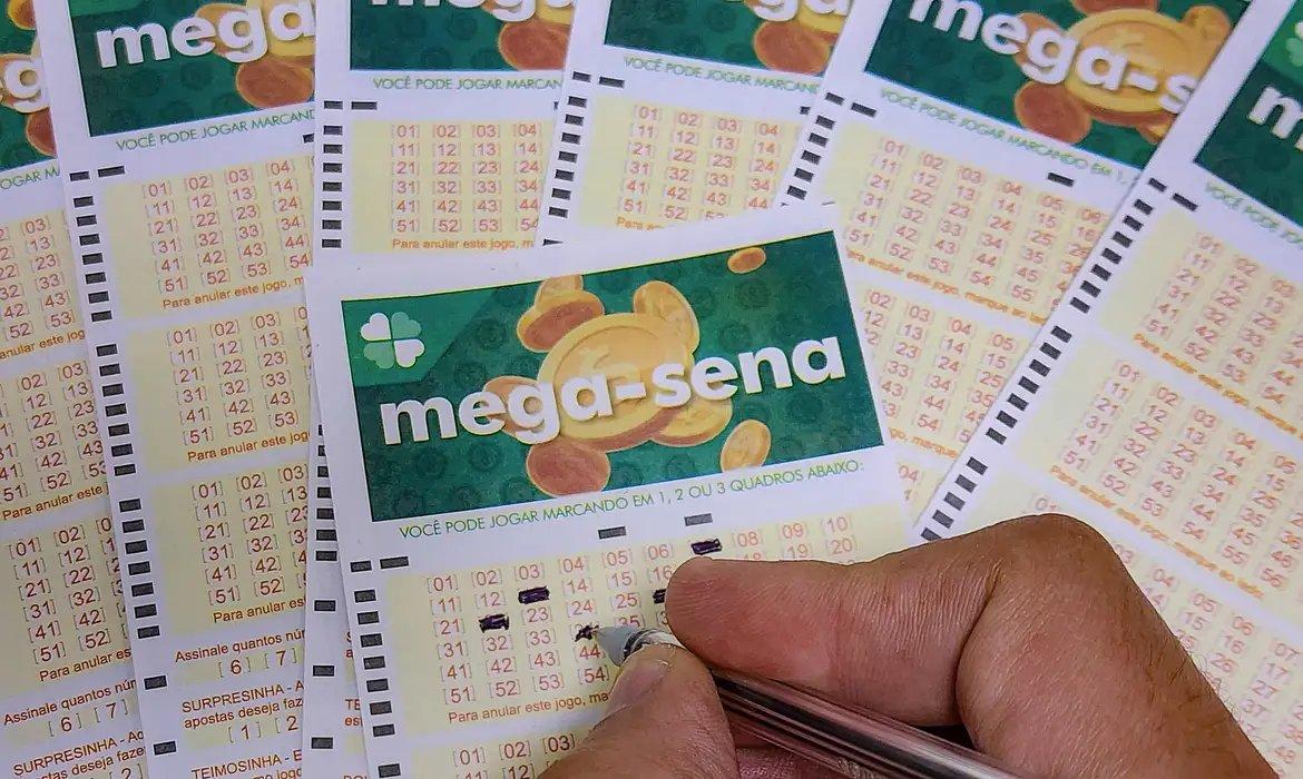 Cartelas de loteria Mega-Sena espalhadas sobre uma mesa, com uma caneta apontando para uma delas, ilustrando loterias da caixa com sorteio.