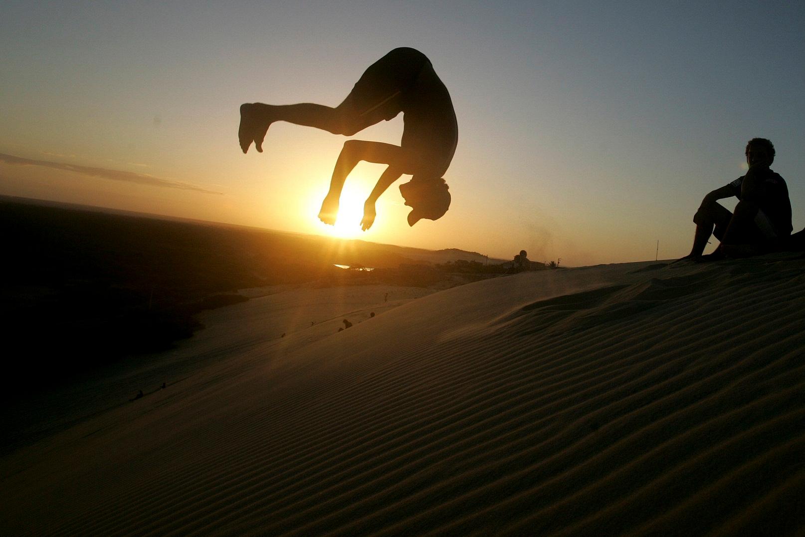 Jovem pratica atividade dando salto mortal na frente do pôr do sol