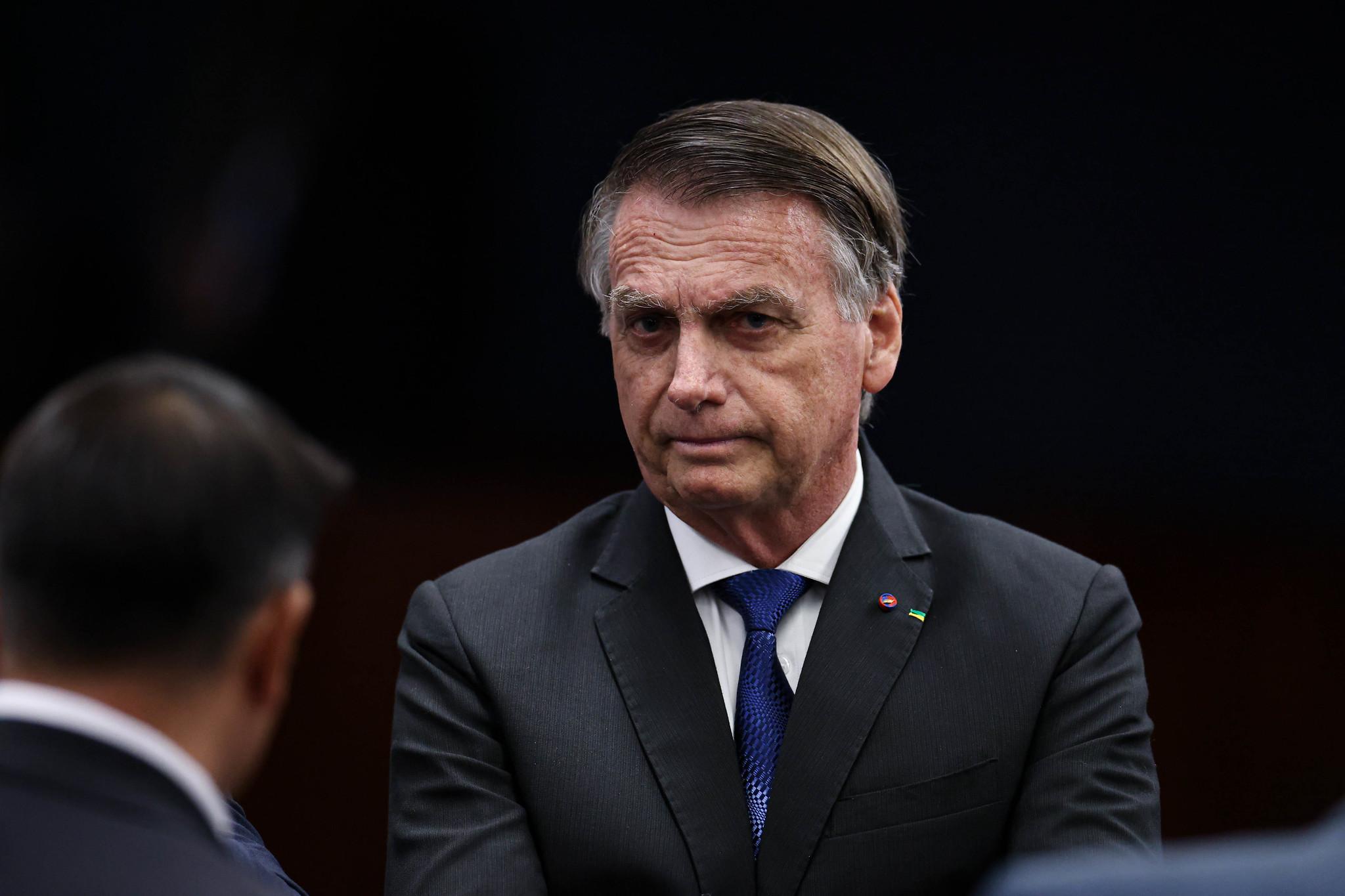 A imagem mostra o ex-presidente Jair Bolsonaro, de terno, olhando para a câmera durante interrogatório da ação penal da tentativa de golpe no STF