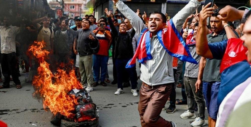 Homem com a bandeira do Netal e pessoas ao retor ateiam fogo em objetos