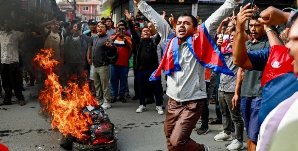 Homem com a bandeira do Netal e pessoas ao retor ateiam fogo em objetos
