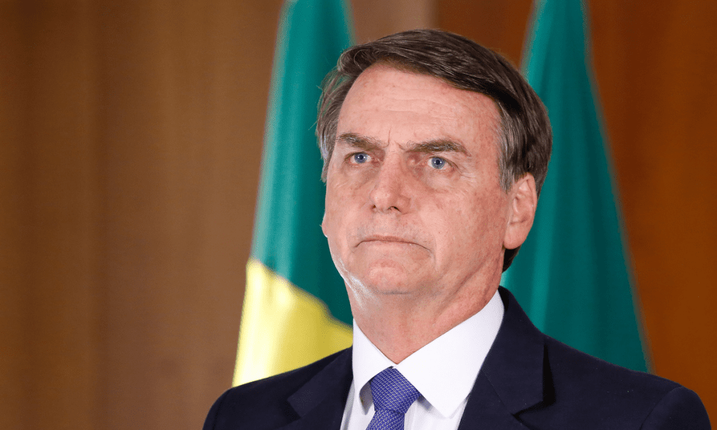 Foto de Jair Bolsonaro, com feição séria, à frente de bandeira do Brasil. Imagem usada para informar que ex-presidente é condenado pelo STF no julgamento da trama golpista
