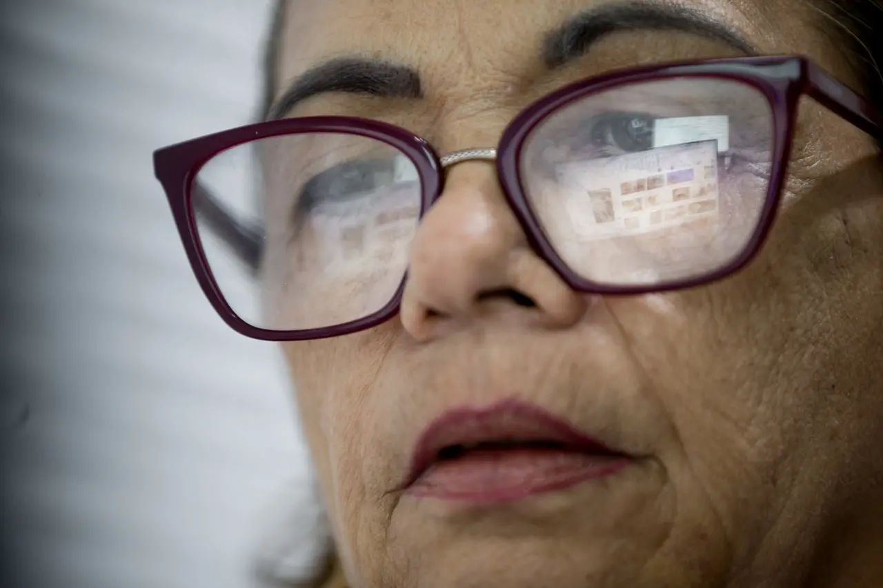 Rosto de mulher de óculos em que tela de computador está refletida nas lentes.
