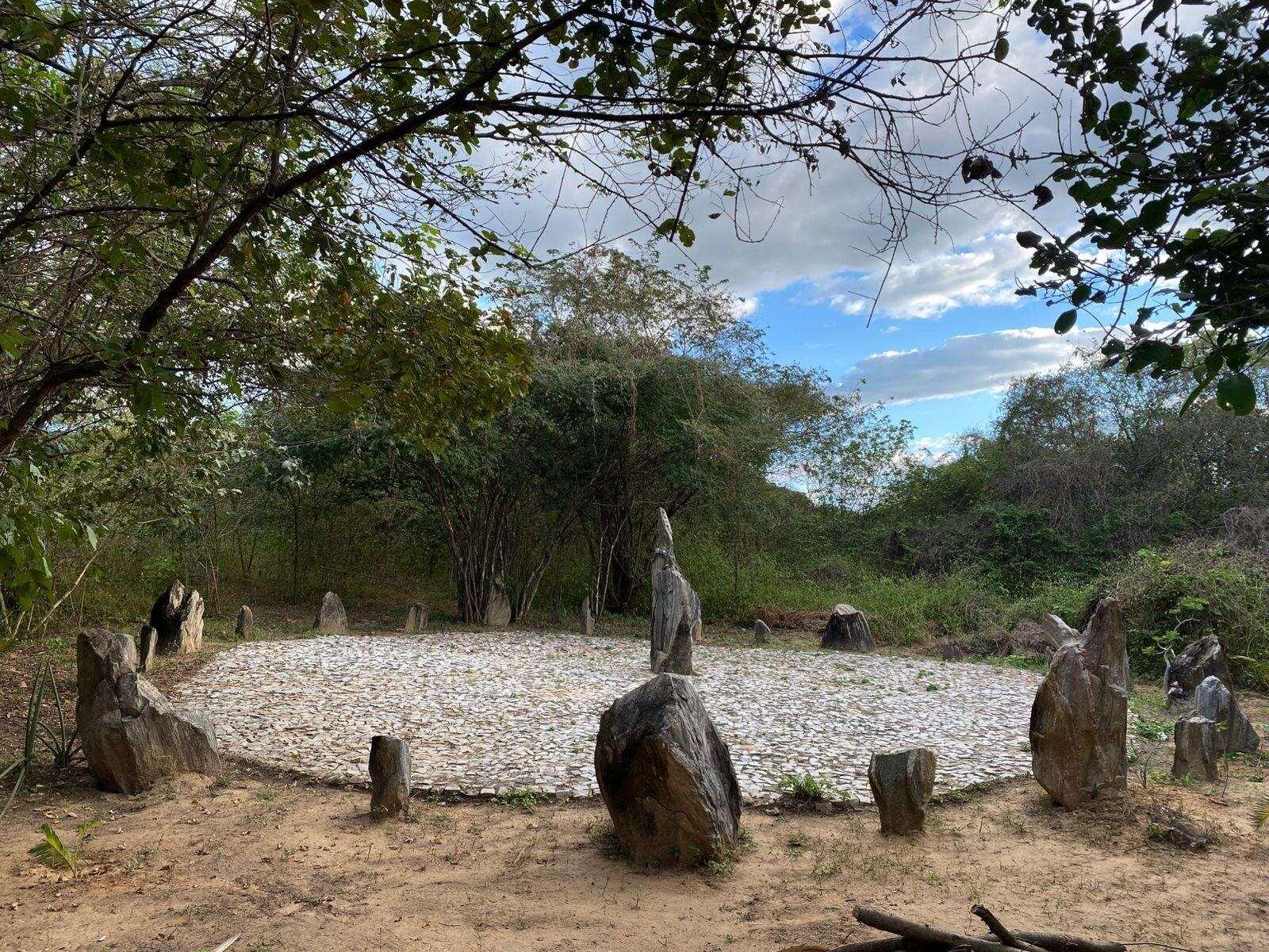 Espaço com estátuas de pedra e círculo destinado ao culto de matriz africana e indígena, cercado de árvores e plantas em Sobral