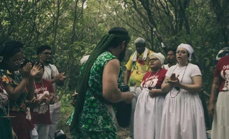 Homens e mulheres com vestes de religiões africanas cantam, batem palmas e dançam durante ritual