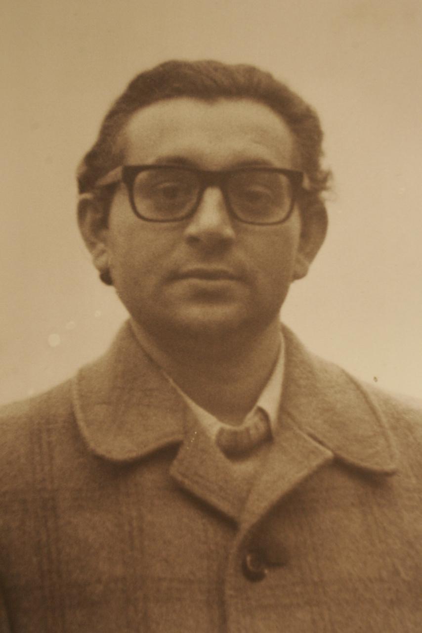 A foto mostra Frei Tito de Alencar, um homem de óculos e cabelo escuro, vestido com um casaco, olhando diretamente para a câmera. Ele tem uma expressão séria. A foto é em sépia ou desbotada, dando a ela uma aparência antiga.