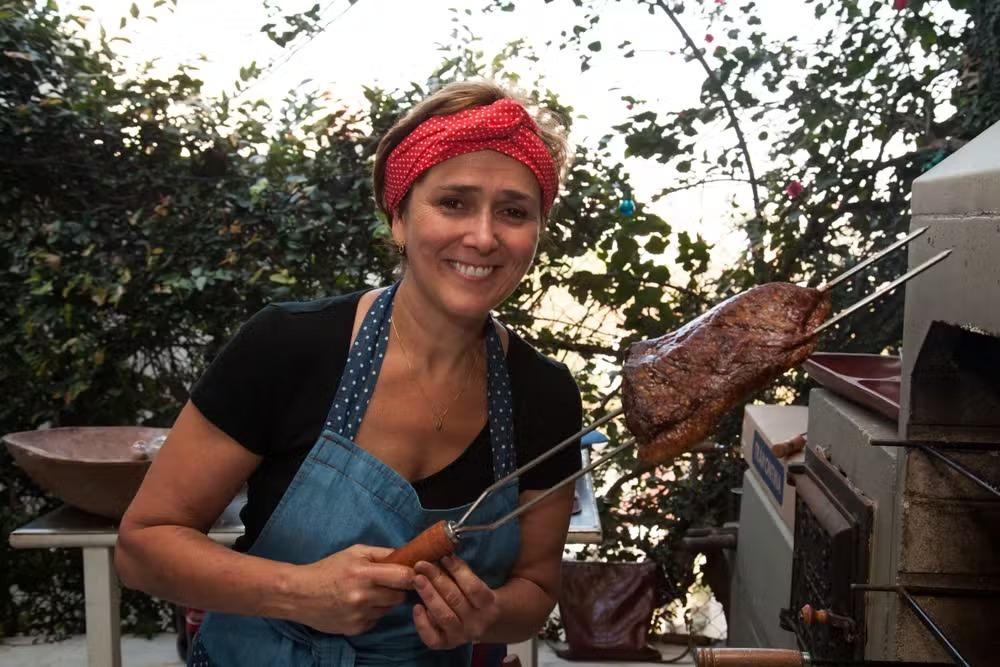 Clarice segurando um espeto de churrasco. Mulher branca de cabelo curto