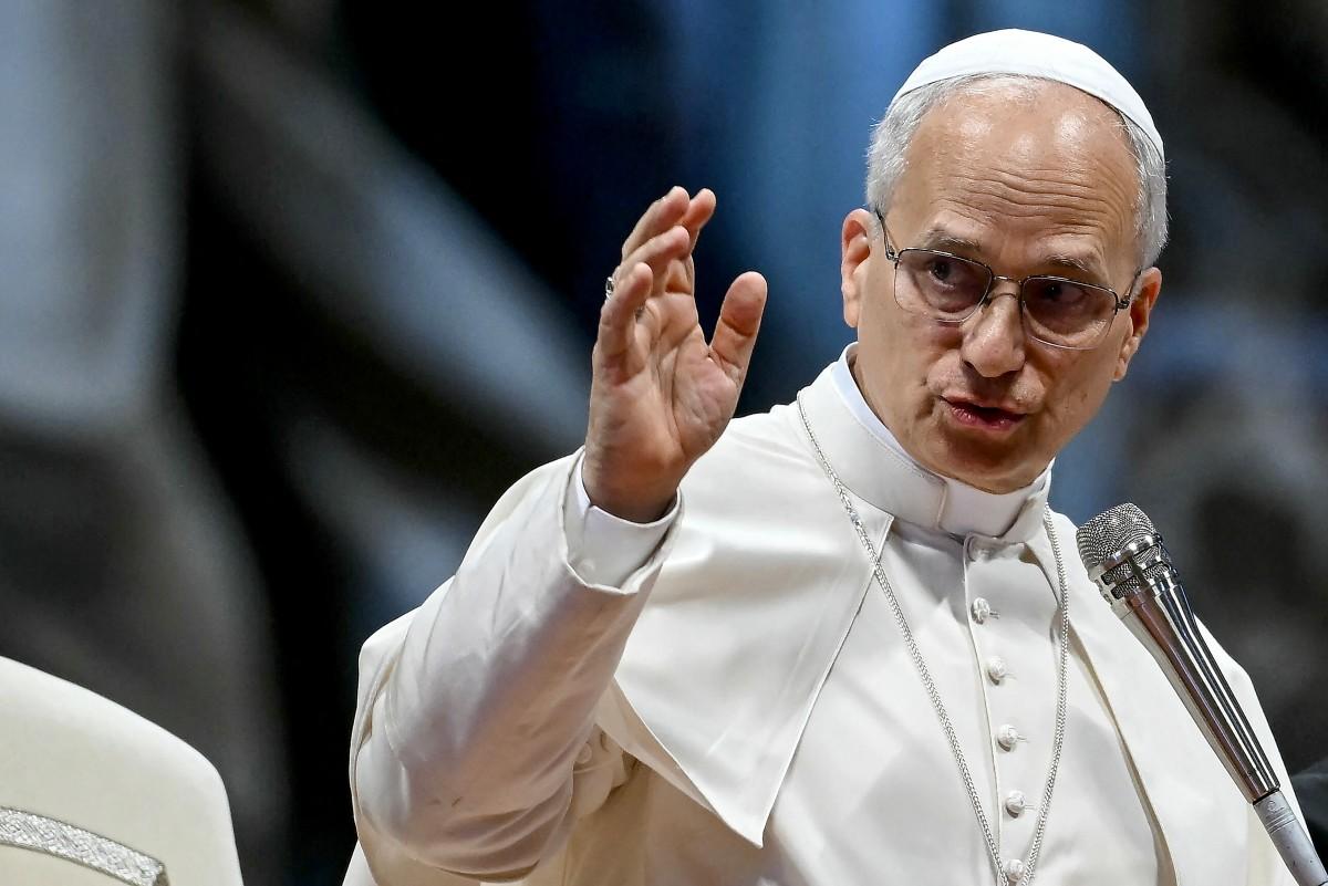 Papa Leão XIV falando em um evento, usando roupa branca e óculos, com expressão séria e gesticulando com a mão