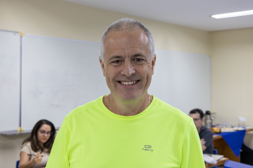 Professor Julio dos Anjos sorri para uma foto. Ele é um homem grisalho, de barba rala e camisa verde