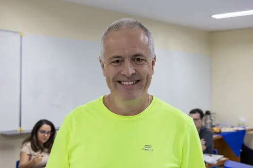 Professor Julio dos Anjos sorri para uma foto. Ele é um homem grisalho, de barba rala e camisa verde