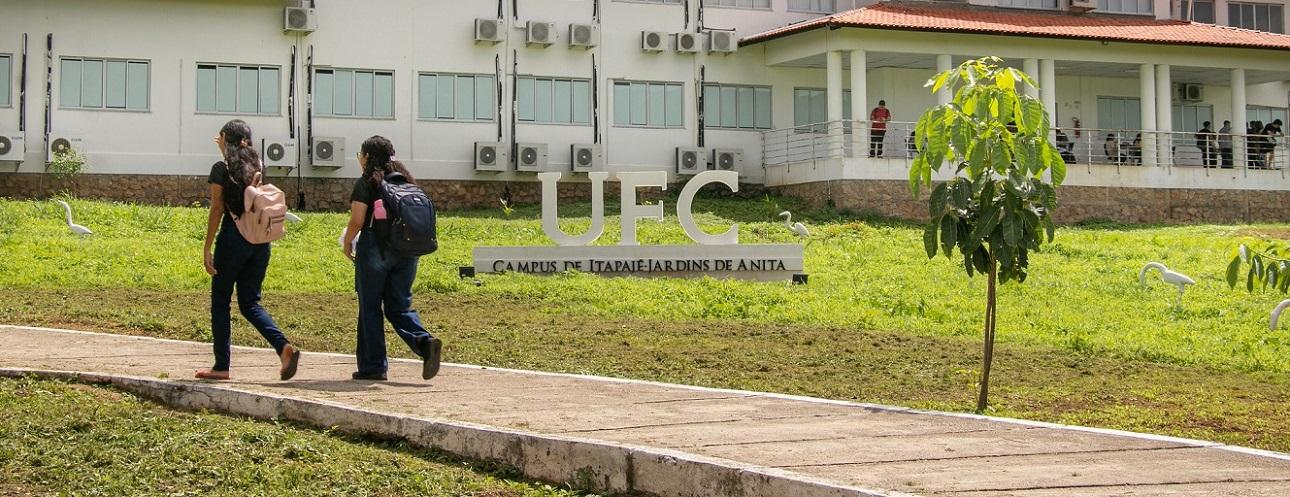 Foto externa do campus da UFC em Itapajé, com gramado e duas alunas com mochilas caminhando