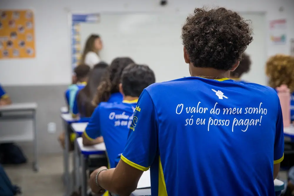 Jovem de costas em primeiro plano vestindo uma farda da escola pública