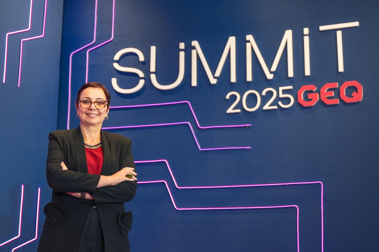 Tânia Cosentino posando em frente a painel azul escrito Summit GEQ 2025