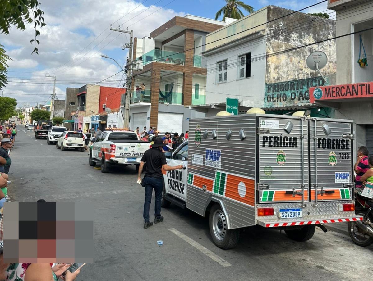 Ocorrência policial em rua movimentada de Sobral, com veículos oficiais da Perícia Forense estacionados e agente uniformizado no local. Pessoas observam a cena com curiosidade. Contexto de assassinado e tentativa de chacina.