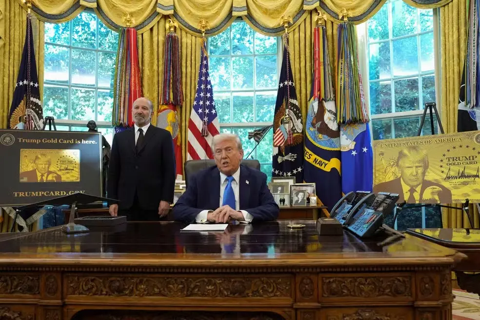 Donald Trump aparece sentado à mesa no Salão Oval da Casa Branca, ao lado de um homem em pé.