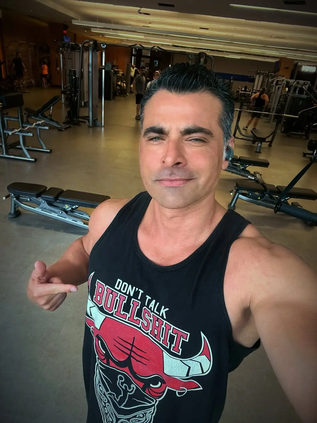 JP Mantovani tirando uma selfie em uma academia enquanto aponta para a blusa que está vestindo