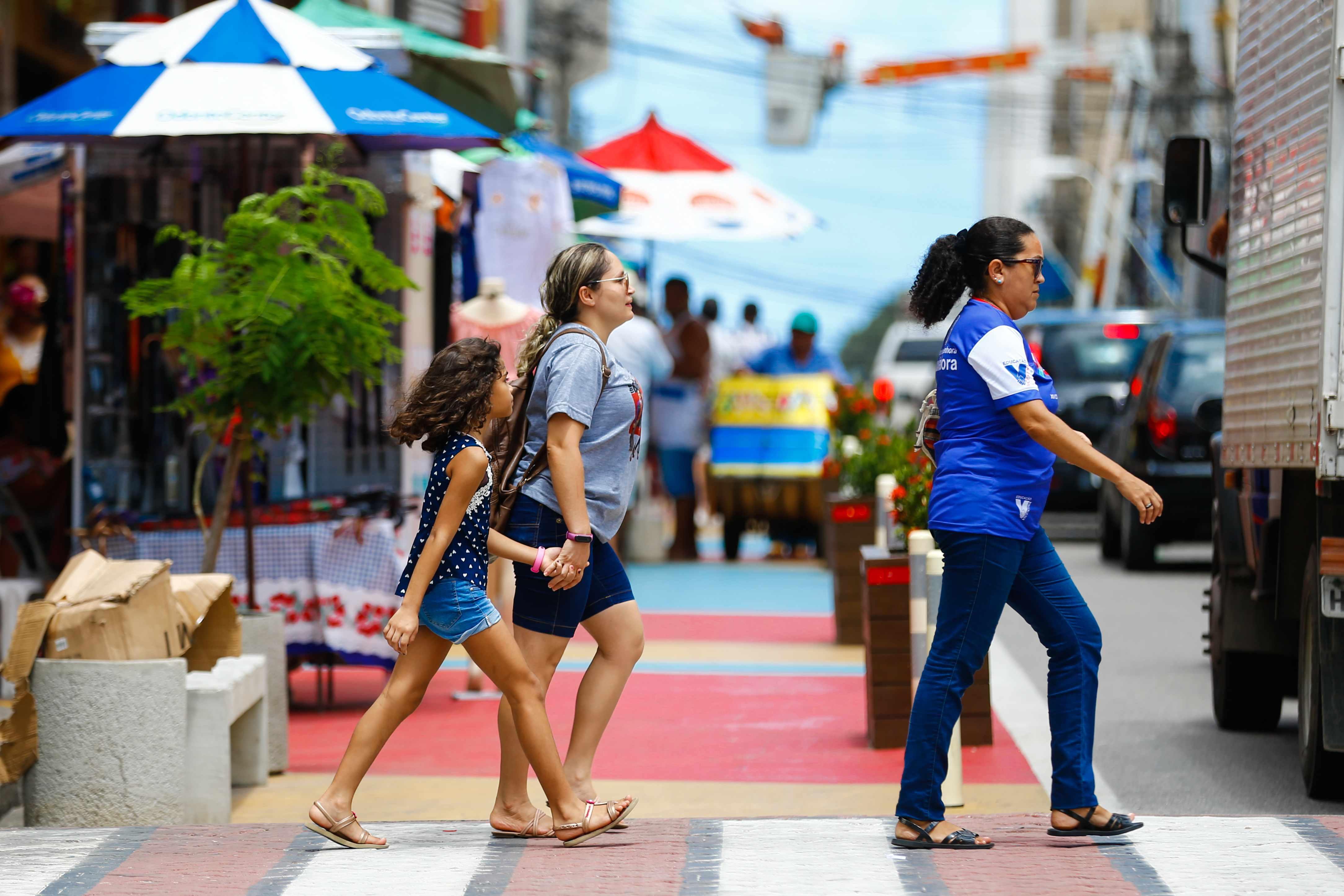 Três mulheres de idades diferentes atravessam a rua no centro de Fortaleza.