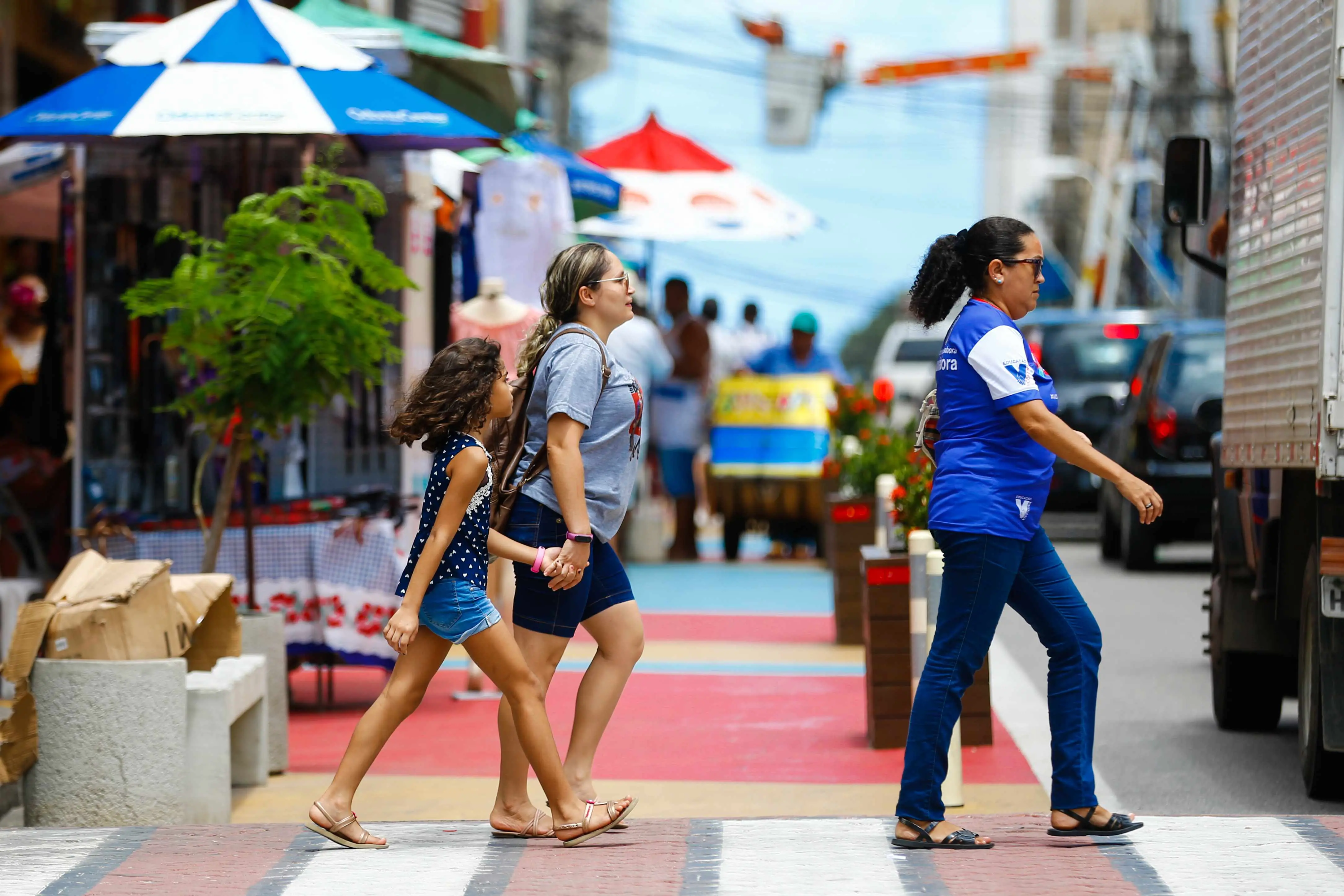 Três mulheres de idades diferentes atravessam a rua no centro de Fortaleza.