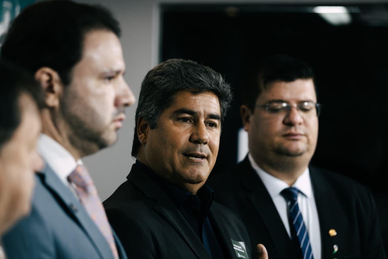 Da esquerda para a direita, em coletiva de imprensa: Léo Couto, presidente da Câmara; Márcio Cardeal, secretário das Finanças; e Bruno Mesquita, líder do Governo Evandro na Câmara. A imagem mostra três homens vestidos com ternos e gravatas em um ambiente formal. O homem ao centro, de cabelos grisalhos e expressão séria, está falando, enquanto os outros dois, à esquerda e à direita, ouvem atentamente. O fundo é neutro, sugerindo um espaço interno institucional.
