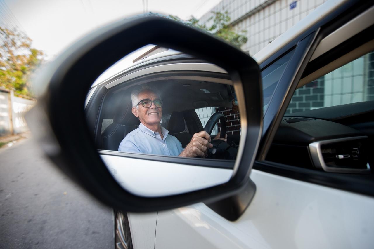 Rosto de homem idoso aparecendo no retrovisor de um veículo.