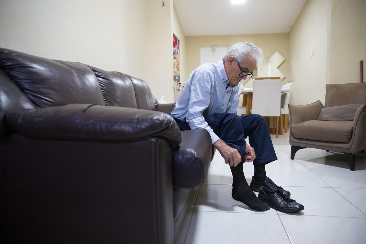 Homem idoso calçando meias e sapatos.