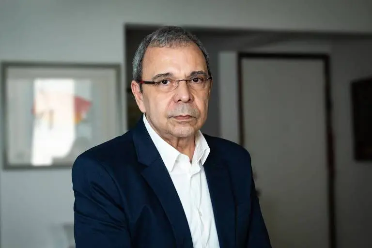 Historiador e professor da UFRJ, Carlos Fico. Ele usa óculos, camisa branca e blazer azul escuro, olhando sério para a câmera em ambiente interno.