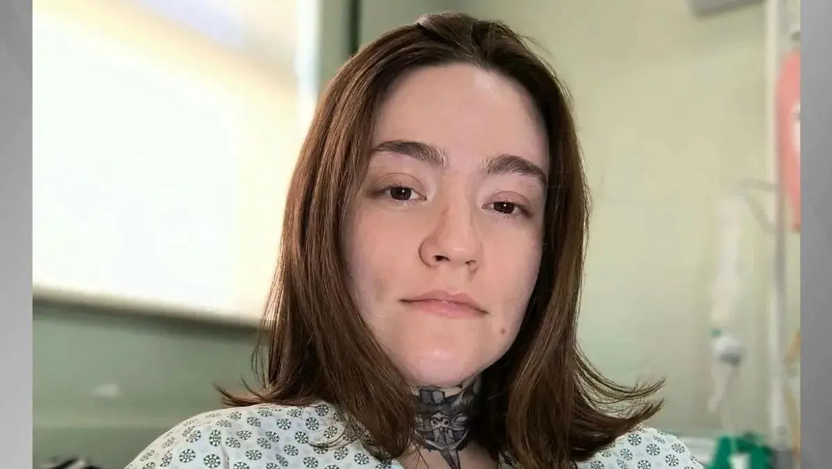 Carolina Arruda com expressão neutra em ambiente hospitalar, vestindo bata médica.