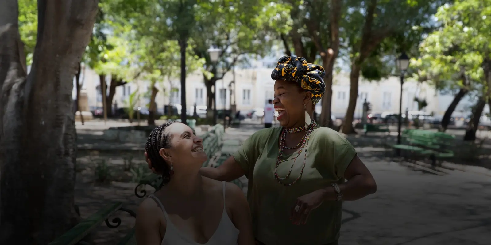 Trancista e cliente com cabelos trançados rindo uma para a outra em uma praça