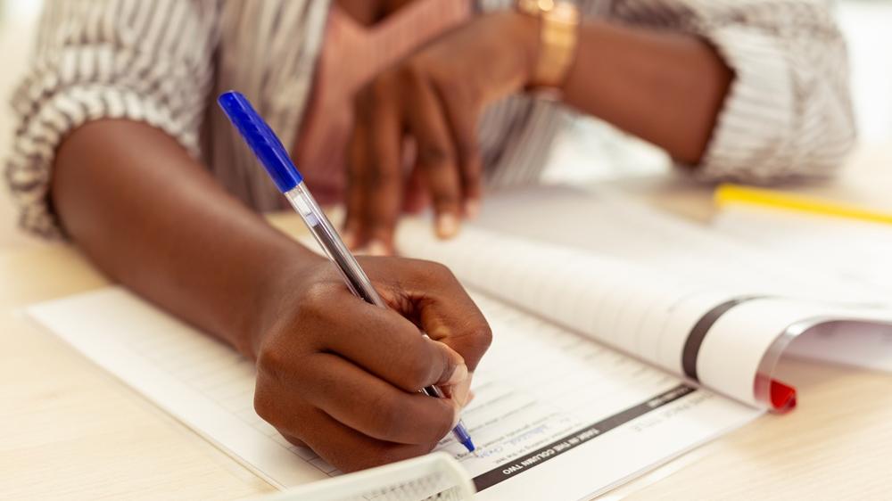 imagem ilustrativa que mostra a mãe de uma pessoa negra segurando uma caneta azul com uma prova