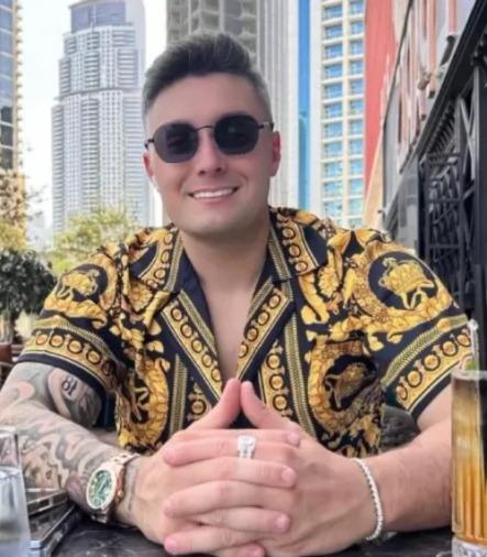 Gabriel Spalone é um homem jovem, branco, de cabelo preto e que usa óculos escuros e camisa amarela estampada.