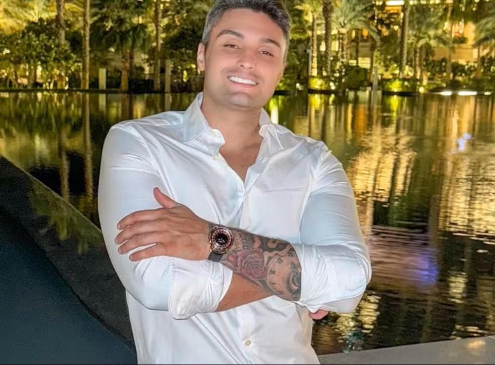 Foto do influenciador Gabriel Spalone, preso por esquema ilegal de Pix, sorrindo, de blusa social branca e braços cruzados.