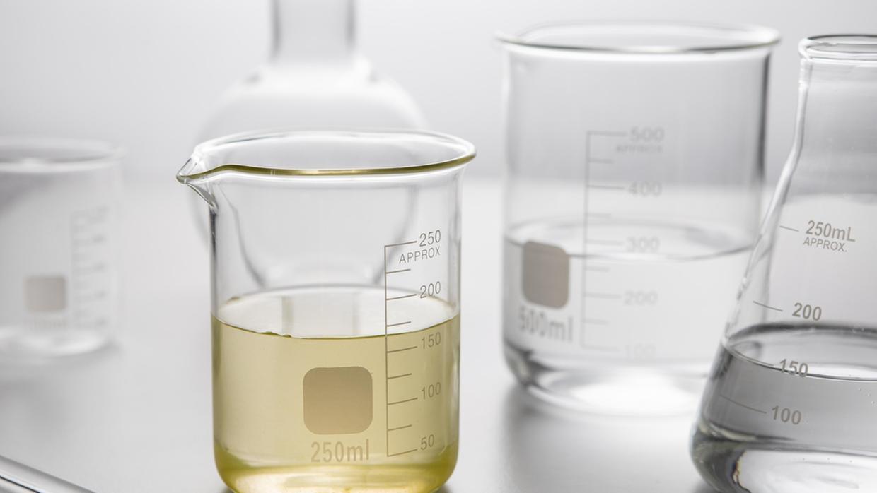 Imagem mostra recipientes transparentes semelhantes aos de um laboratório com líquido translúcido amarelado, o metanol, em um fundo branco.