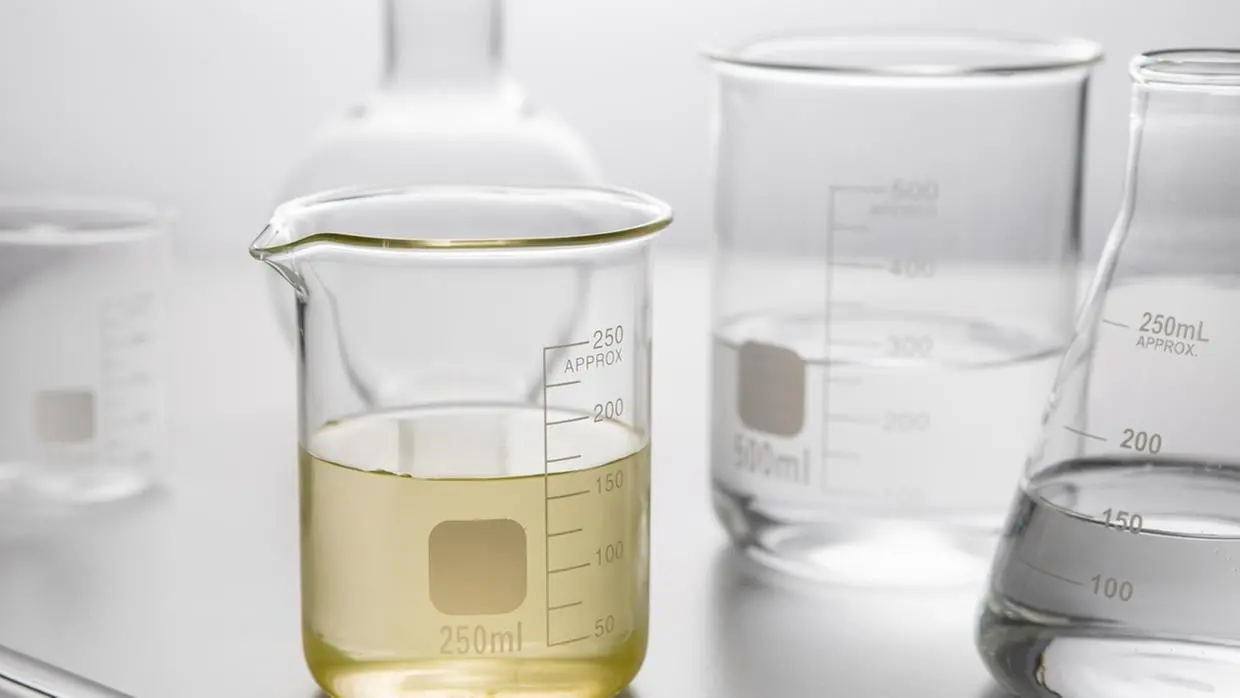Imagem mostra recipientes transparentes semelhantes aos de um laboratório com líquido translúcido amarelado, o metanol, em um fundo branco.