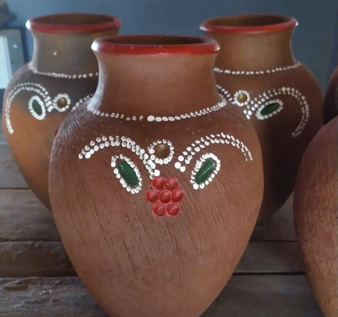 Vasos de barro em tom marrom, com bordas avermelhadas e detalhes pintados à mão em branco, verde e vermelho, formando desenhos florais e geométricos decorativos.