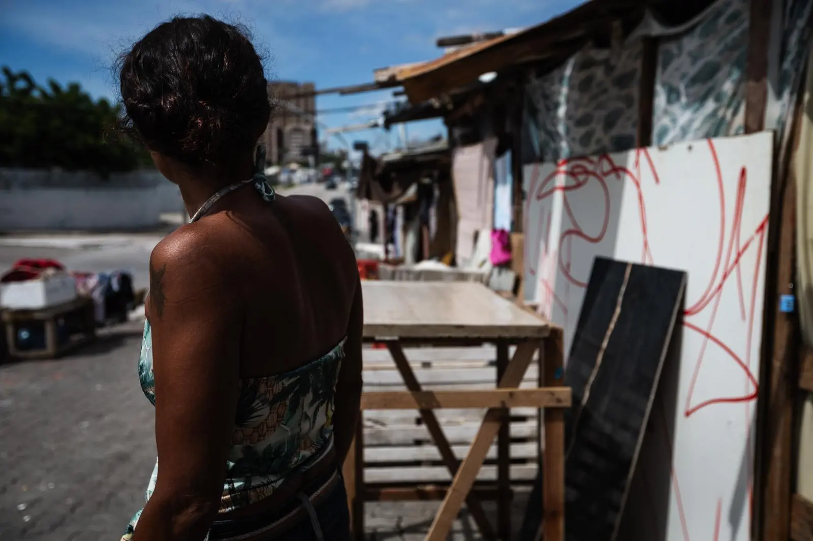 Mulher de costas olha para extensão da rua repleta de barracos de madeira e papelão em Fortaleza