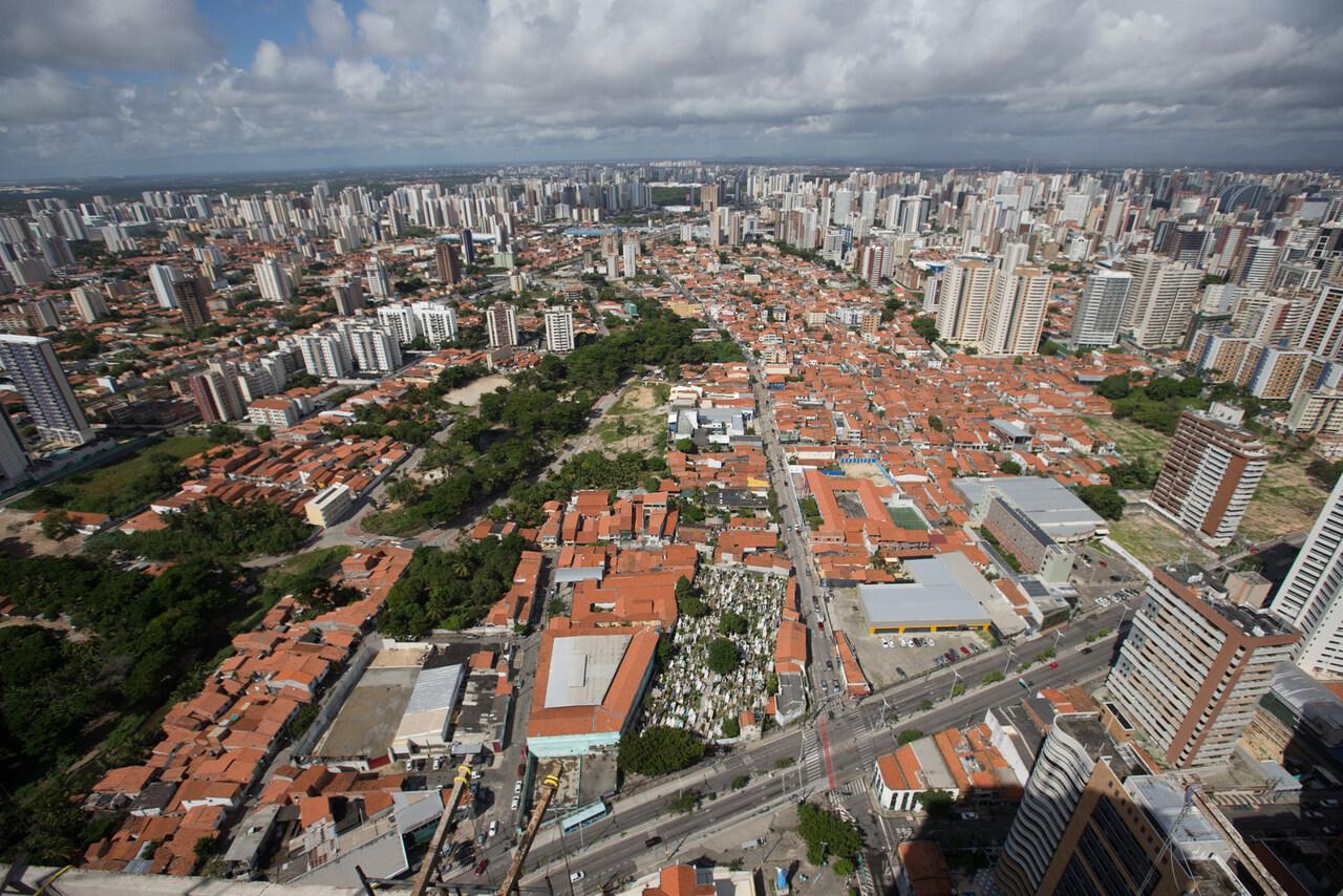 Imagem mostra vista aérea de Fortaleza, com telhados de casas e apartamentos, além de outros estabelecimentos. Também é possível ver ruas, avenidas e um pouco da vegetação.