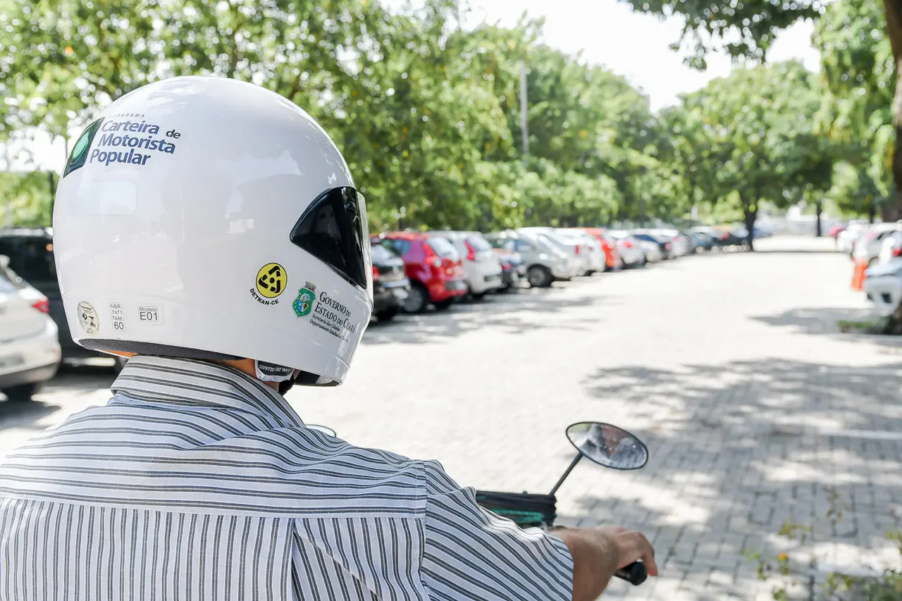Foto mostra motociclista contemplado pelo programa CNH Popular com capacete e carteira de habilitação