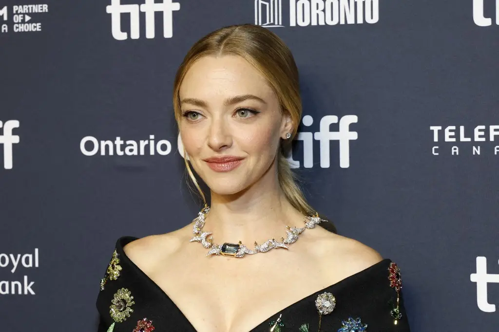 Amanda Seyfried em foto de close do rosto. Ela aparece com cabelos presos e vestido preto