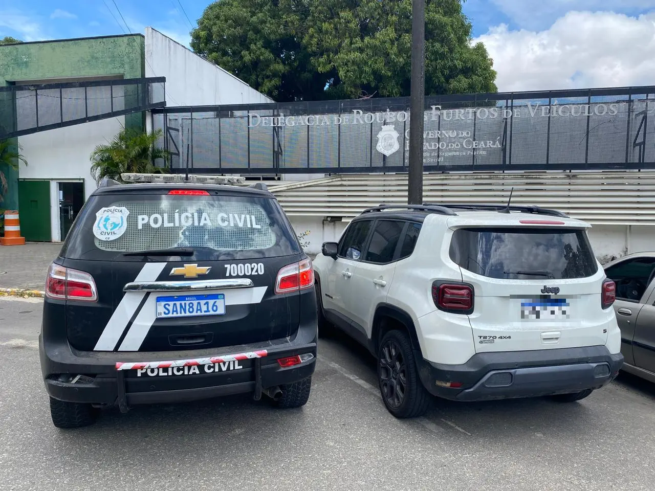 Foto mostra uma viatura da Polícia Civil do Ceará, ao lado de um veículo Jeep Renegade branco, recuperado pela Polícia. Os dois carros estão em frente à Delegacia de Roubos e Furtos de Veículos, em Fortaleza