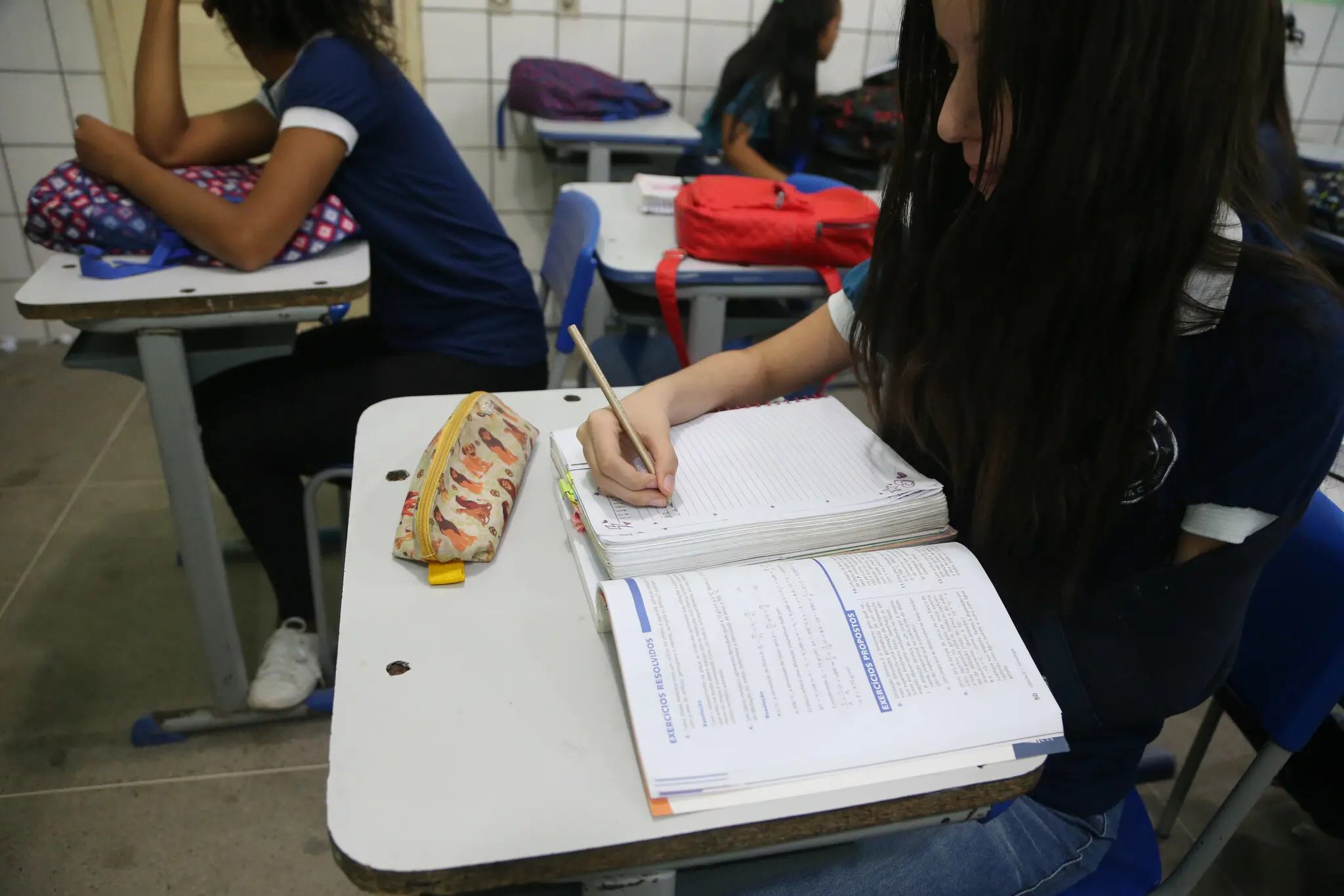 Aluna escrevendo em caderno durante a aula.
