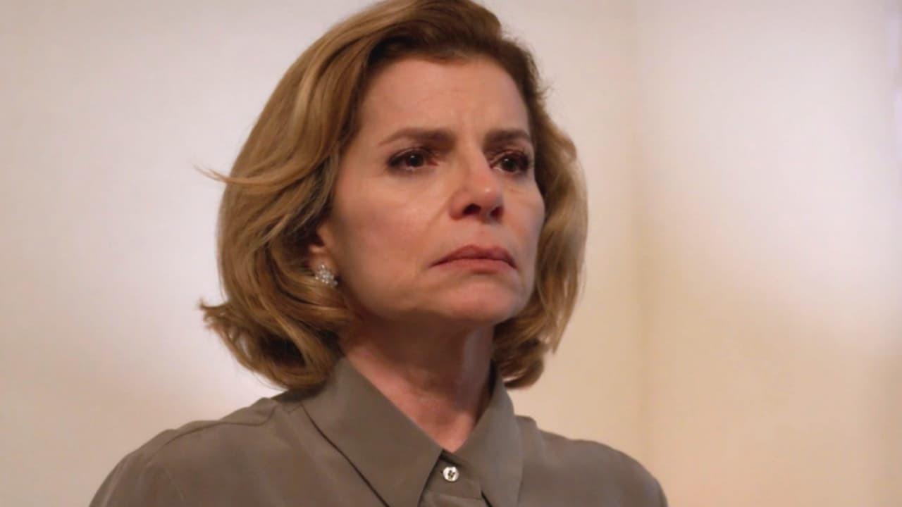 Mulher da terceira idade, branca, loira de cabelo curto e liso, com expressão triste. Usa terno cinza visível até o ombro, em cenário com fundo de parede branca.