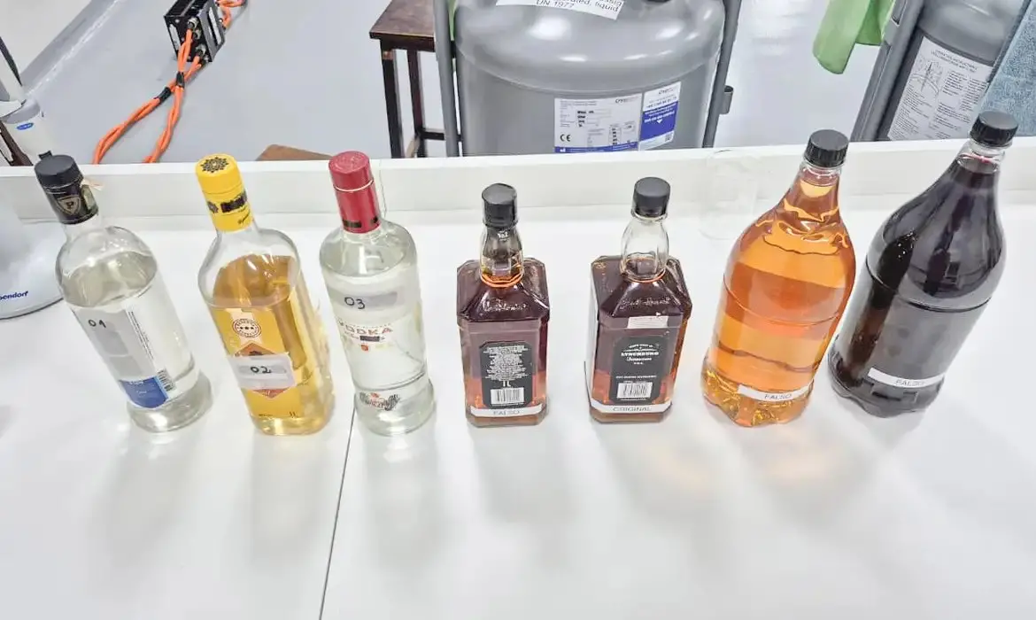 Imagem mostra diferentes garrafas de bebidas alcoólicas sobre uma mesa, incluindo vodka, whisky, tequila, rum e licor.